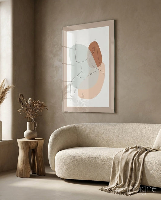 Framed glass wall art featuring sage green and terracotta line drawing of woman displayed above cream curved sofa in minimalist interior.