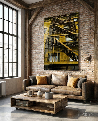 Yellow and black fire escape staircase glass wall art displayed above tan leather sofa in industrial loft interior.