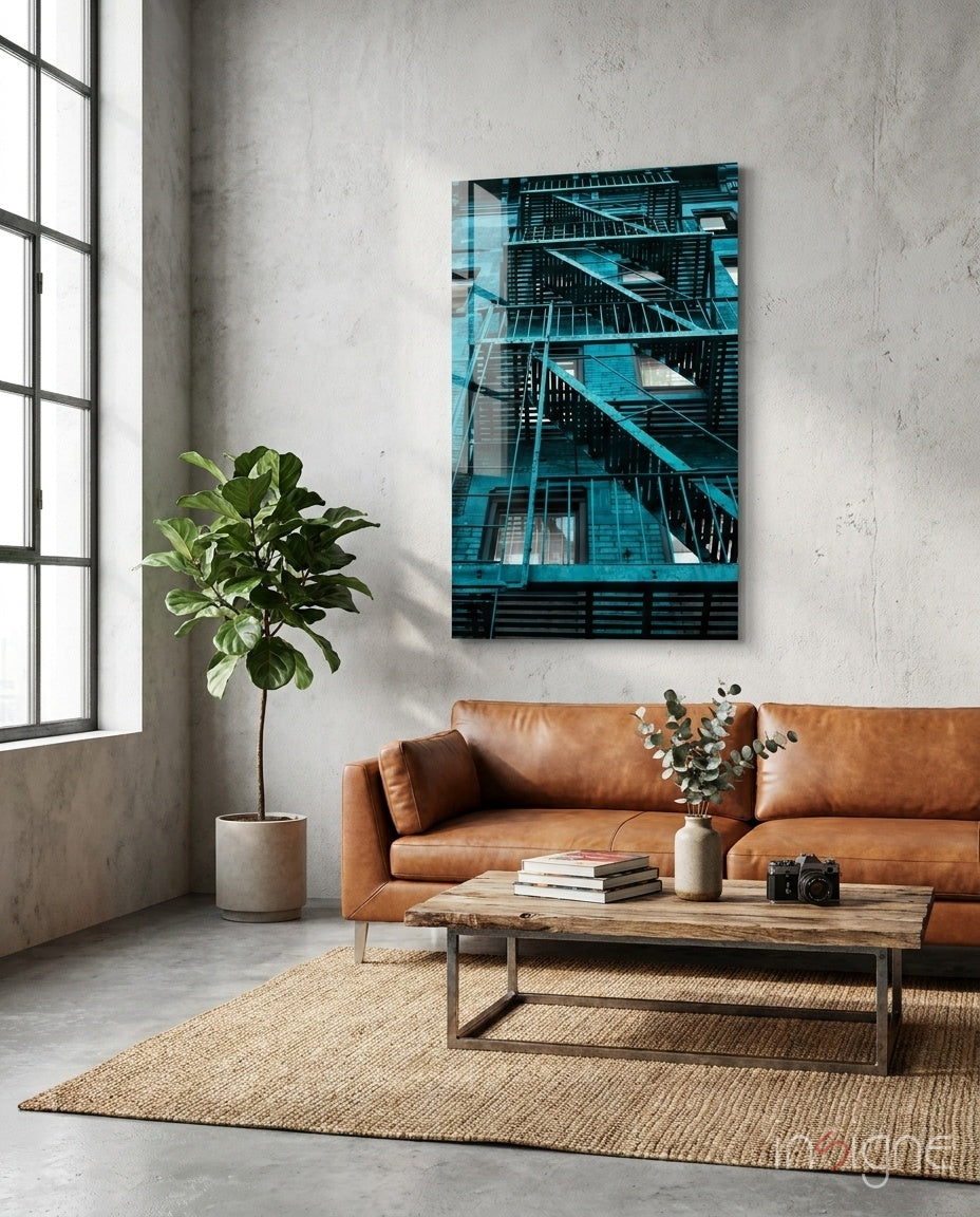 Blue Stairs glass wall art depicting turquoise fire escape stairs displayed above tan leather sofa in industrial loft setting.