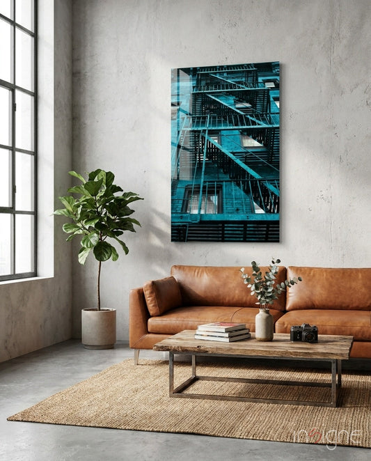 Blue Stairs glass wall art depicting turquoise fire escape stairs displayed above tan leather sofa in industrial loft setting.