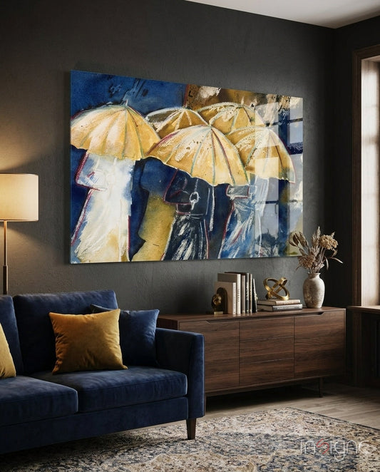 Watercolor painting of figures holding yellow umbrellas against blue background, displayed on dark wall above navy chair and wooden dresser.