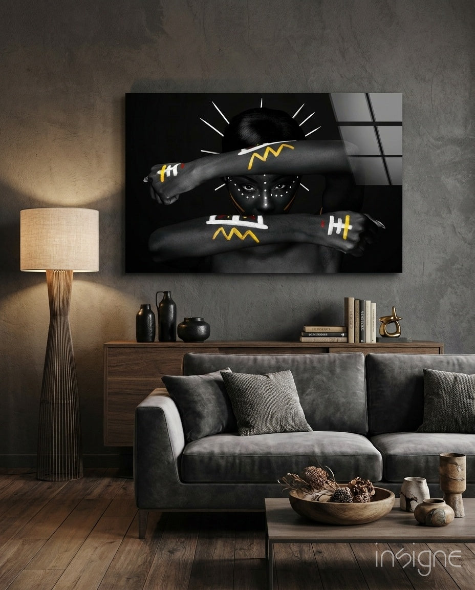 Native American glass wall art displaying figure with crossed arms bearing yellow lightning bolt designs, hung above gray sofa in modern living room.