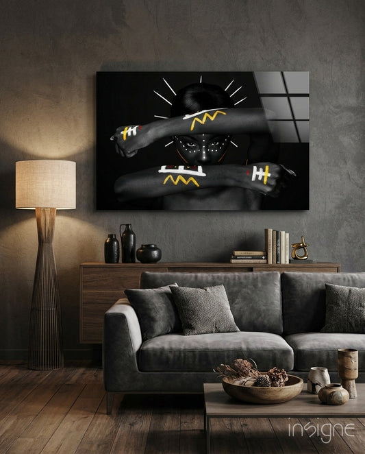 Native American glass wall art displaying figure with crossed arms bearing yellow lightning bolt designs, hung above gray sofa in modern living room.