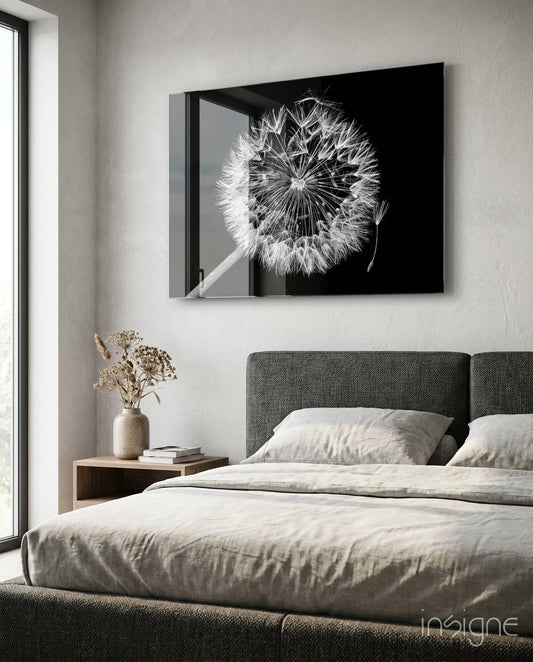 Black glass wall art depicting a detailed dandelion seedhead in white against dark background, hung above a bedroom bed with gray headboard.