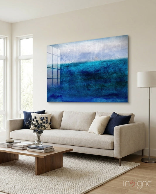 Blue gradient glass wall art with layered ocean-toned colors displayed above a beige sofa in a modern living room.