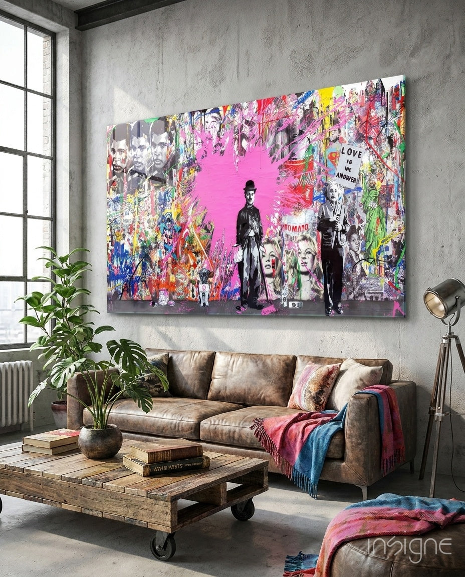 Colorful pop art glass wall panel featuring silhouettes and portraits with pink background displayed above brown leather sofa in industrial loft interior.