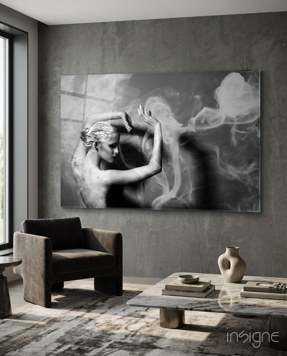 Black and white glass wall art depicting a sculptural figure with smoke effects, displayed in a modern concrete interior above a chair.