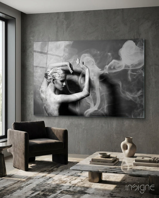 Black and white glass wall art depicting a sculptural figure with smoke effects, displayed in a modern concrete interior above a chair.
