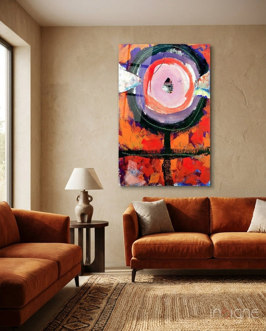 Vibrant abstract glass wall art with concentric circles in orange, pink, and black displayed above a rust-colored sofa in a modern living room.