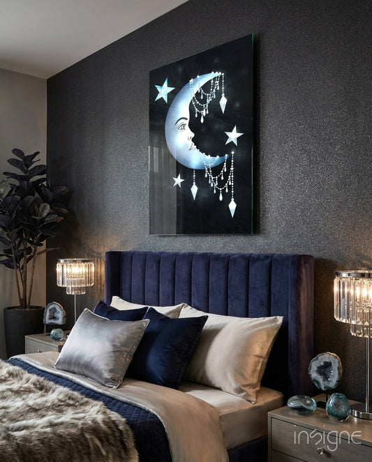 Moon and stars glass wall art with hanging crystals displayed above navy blue upholstered bed in dark bedroom.