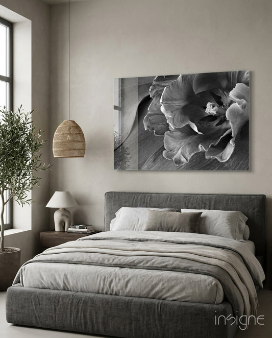 Black and white glass wall art of tulip flowers displayed above a gray upholstered bed in a minimalist bedroom.