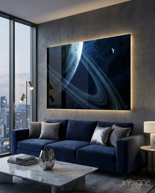 Backlit glass wall art depicting a blue ringed planet with rings and moons in space, displayed above a navy sofa in a high-rise apartment.