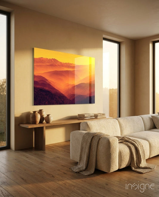 Warm landscape glass wall art displaying layered mountains in orange and yellow tones, mounted above wooden console table in modern living room setting.