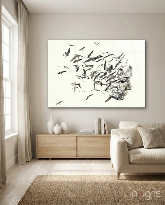 Monochrome glass wall art depicting a profile head dissolving into flying birds, displayed above wooden cabinet in minimalist living room.
