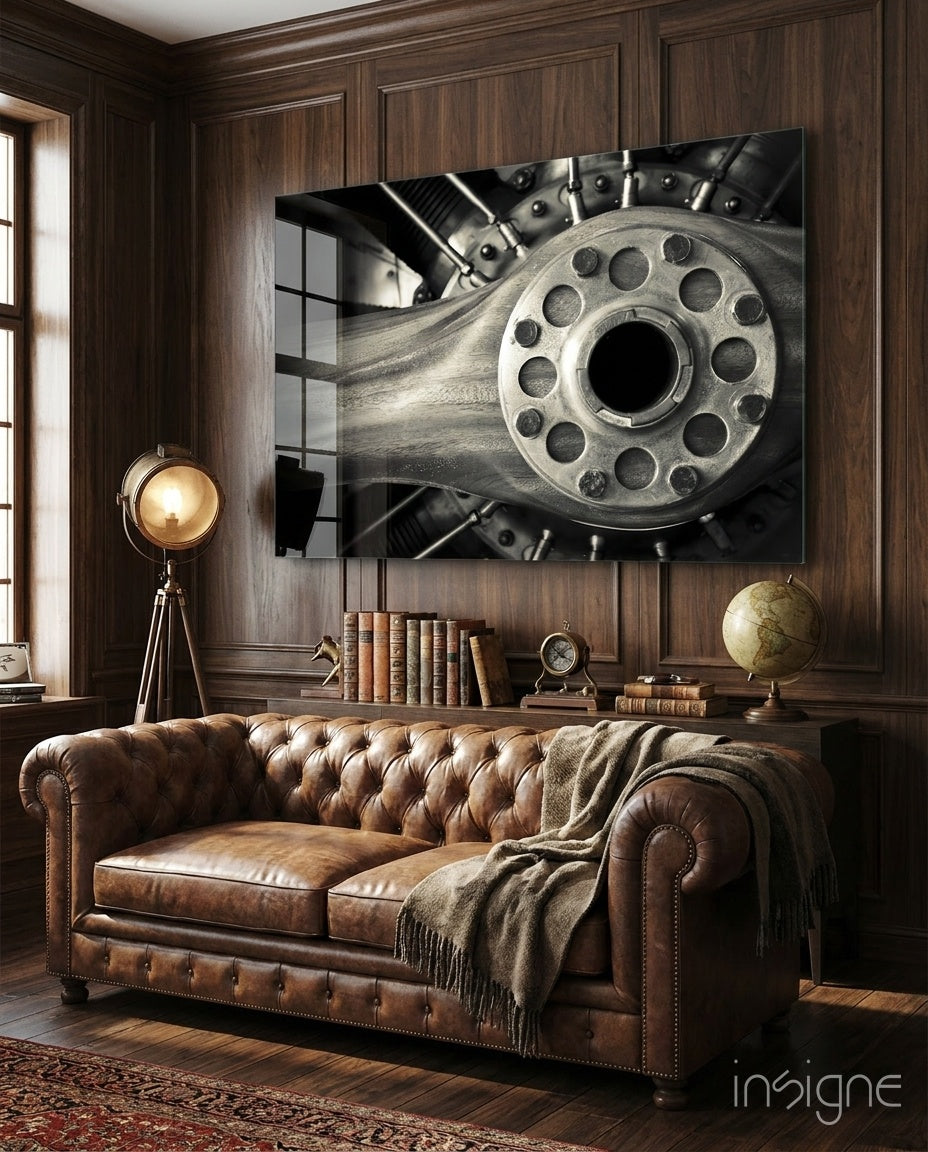 Monochromatic glass wall art depicting a close-up revolver cylinder displayed above a brown leather Chesterfield sofa in a wood-paneled study.
