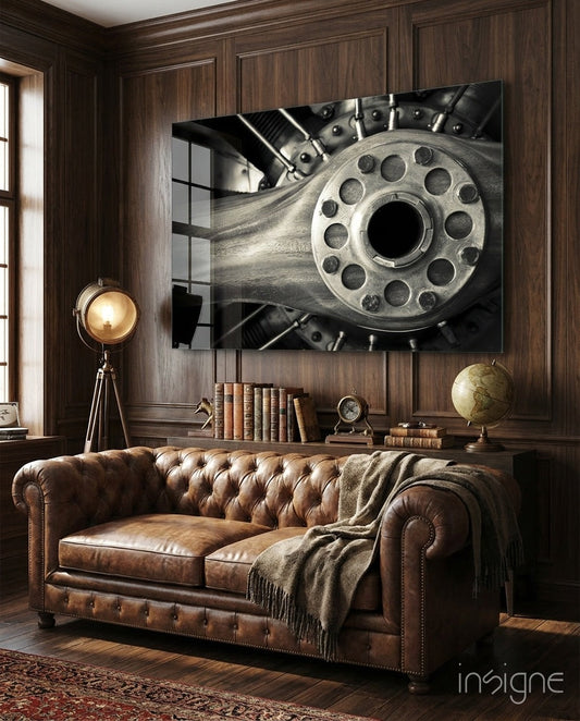 Monochromatic glass wall art depicting a close-up revolver cylinder displayed above a brown leather Chesterfield sofa in a wood-paneled study.