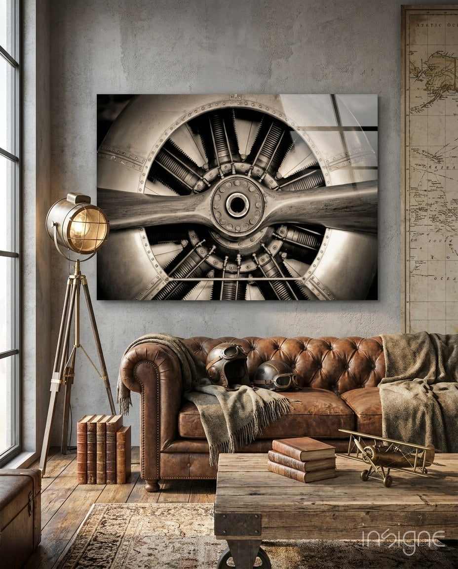 Sepia-toned aircraft propeller engine glass wall art displayed above a leather chesterfield sofa in an industrial-style room with vintage decor.