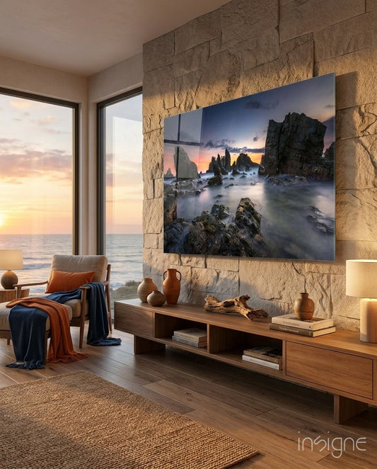 Glass wall art displaying rocky sea stacks at sunset mounted on stone wall in modern coastal living room with ocean view.