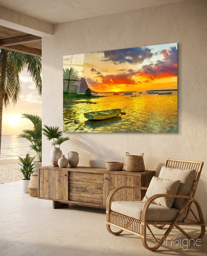 Coastal sunset canvas print displayed above wooden sideboard in beige interior with rattan chair and palm plants.