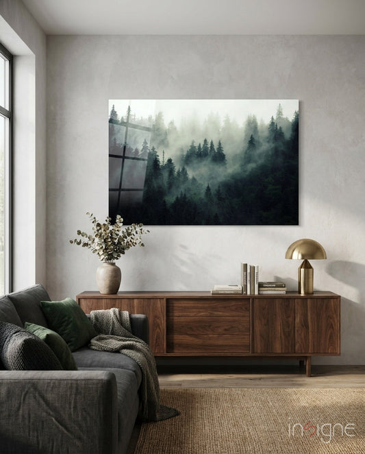 Misty forest landscape glass wall art displaying dark evergreen trees in fog, hung above wooden sideboard in modern living room setting.