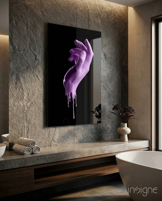 Purple dripping hand sculpture displayed on bathroom mirror above stone countertop with rolled towels and vase.