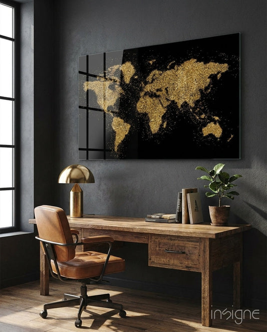 Gold and black world map glass wall art displayed above wooden desk in modern office setting with leather chair and brass lamp.
