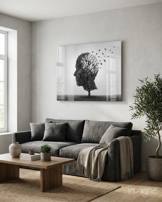 Glass wall art depicting a tree-shaped human head with birds flying away, displayed above a gray sofa in a modern living room.