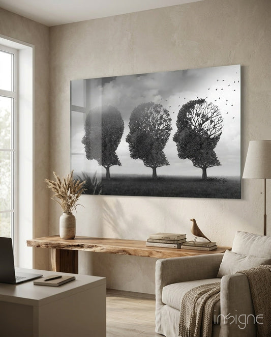 Black and white glass art depicting three tree-shaped head silhouettes with dispersing leaves, displayed above wooden console in modern living room.