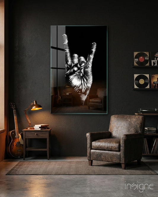 Black and white glass wall art depicting a hand making a rock horns gesture, displayed in a modern music room setting above a leather chair.
