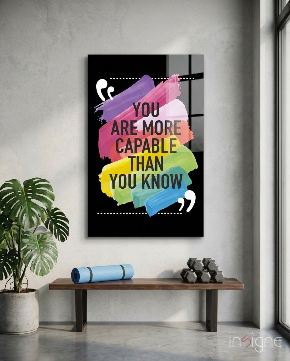 Motivational glass wall art with colorful paint strokes and dark text hanging above wooden bench with plant and dumbbells.