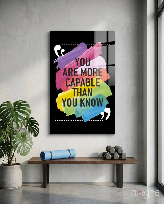 Motivational glass wall art with colorful paint strokes and dark text hanging above wooden bench with plant and dumbbells.