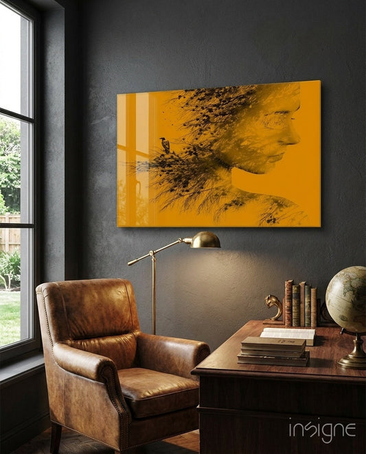 Amber glass wall art featuring a woman's profile with bird and tree silhouettes displayed above a leather chair in a modern study.