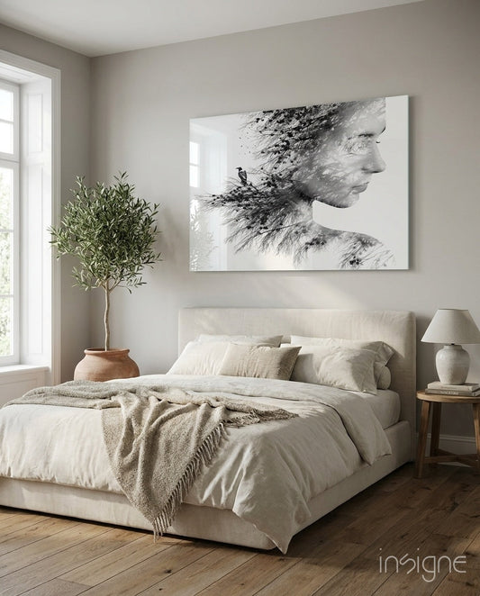 Black and white double exposure glass wall art of woman's profile with forest and bird imagery, displayed above cream bed in minimalist bedroom.