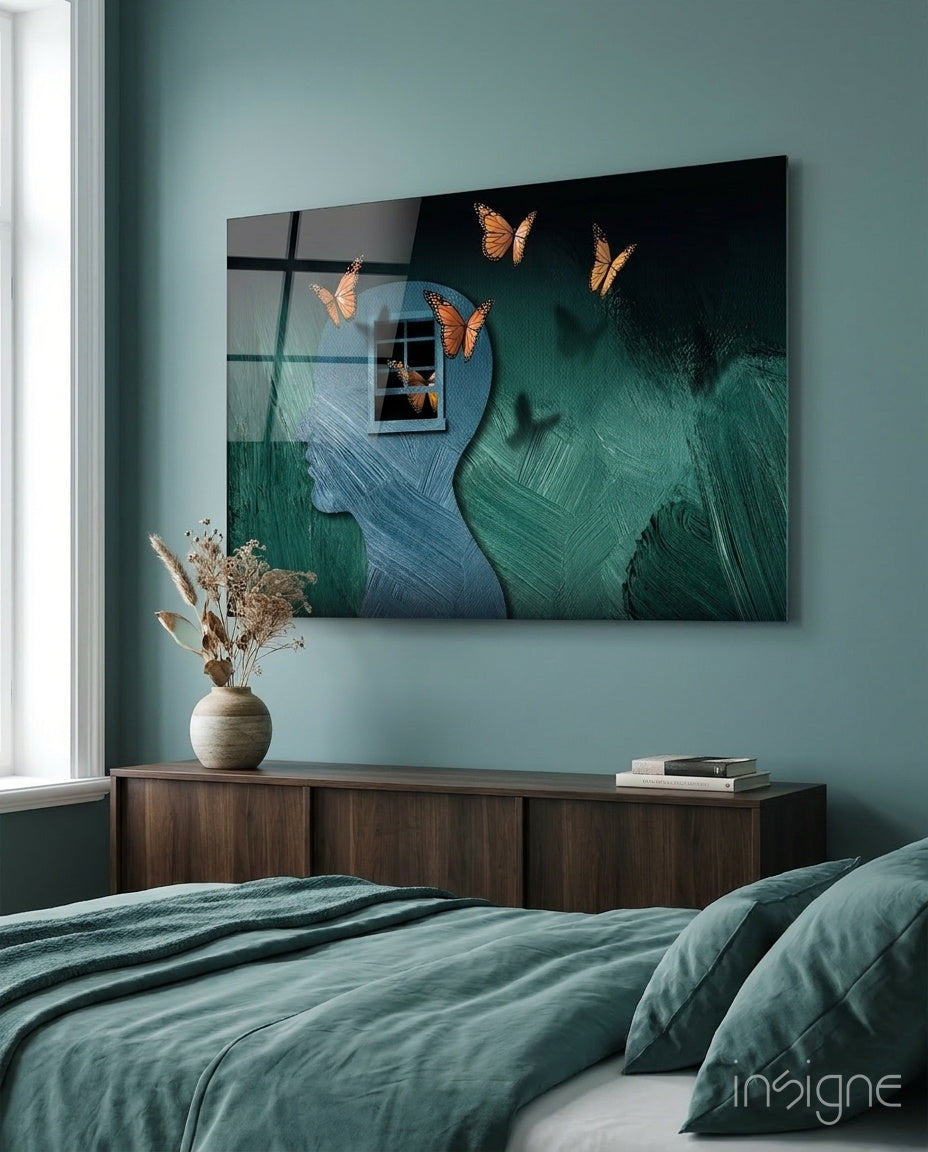 Butterfly Effect Glass Wall Art mounted above wooden dresser in teal bedroom, showing profile silhouettes with monarch butterflies and window reflections.
