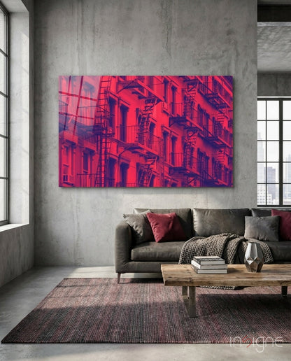 Vibrant neon pink and purple glass wall art depicting an urban building facade with fire escapes, displayed above a gray sofa in an industrial loft interior.