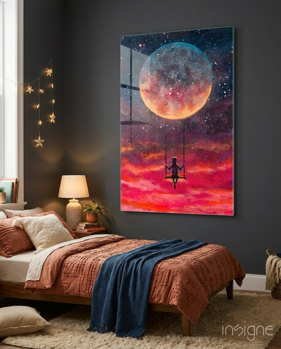 Glass wall art panel depicting a silhouetted figure on a swing against a large glowing moon and fiery red sunset sky, installed above a bedroom bed.