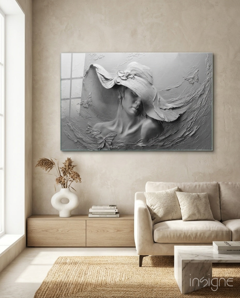 White relief glass wall art depicting a woman wearing a wide-brimmed hat, displayed above a wooden cabinet in a minimalist living room.