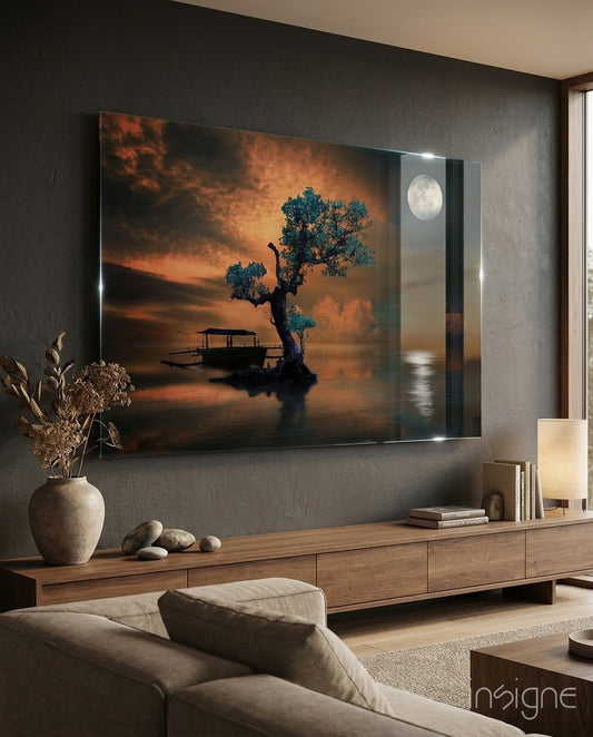 Framed glass wall art mounted above wooden console displaying turquoise tree, moonlit lake, boat, and orange sunset sky in modern living room setting.