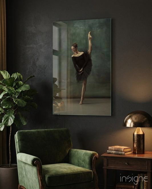 Vertical glass wall art depicting a ballerina in black tutu with raised arm, displayed above green velvet chair in modern interior setting.