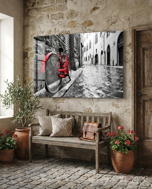Red bicycle glass art displayed on rustic stone wall above wooden bench with potted flowers.