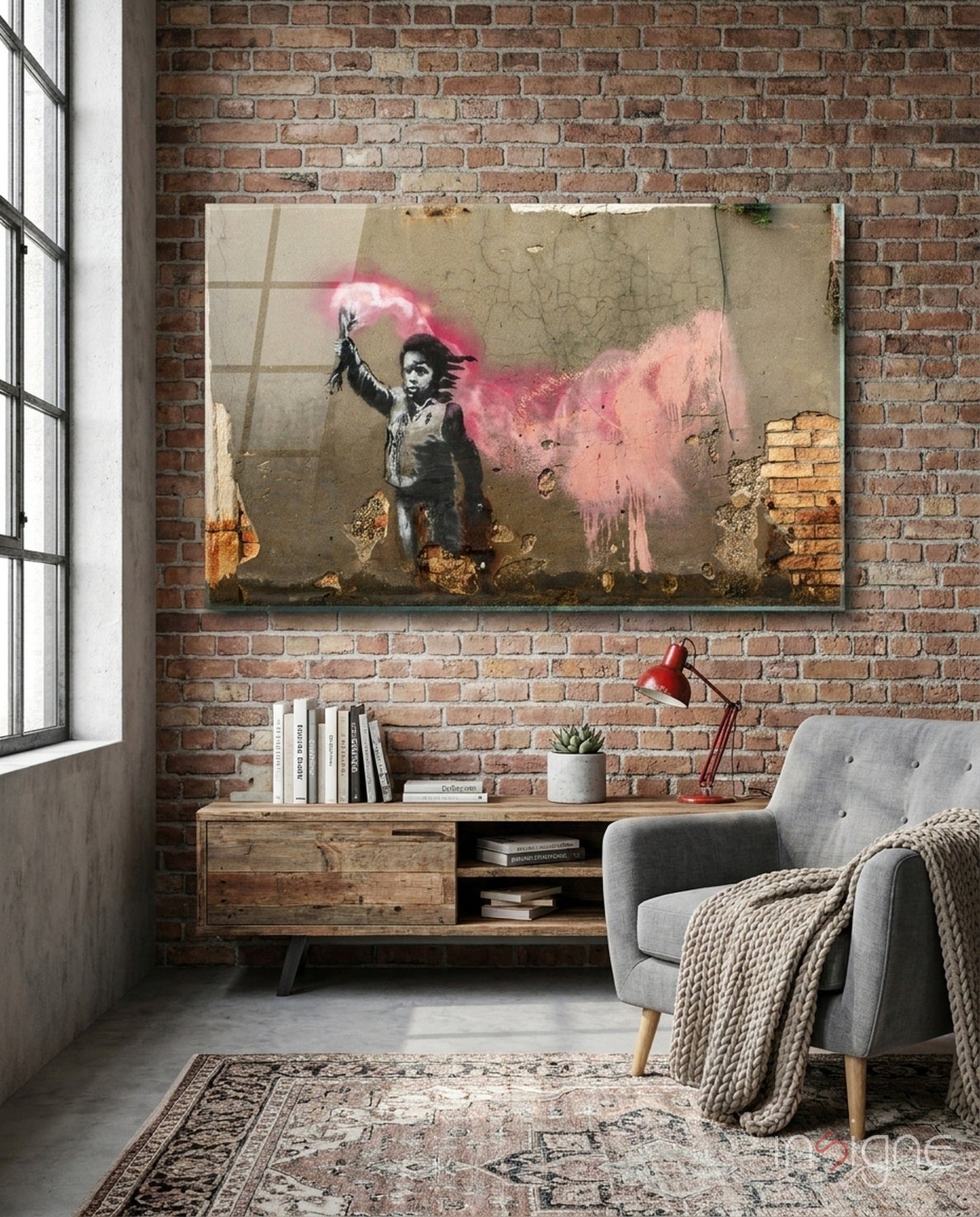 Glass art print hung on brick wall above wooden desk in loft room, showing stenciled child figure with pink powder explosion.