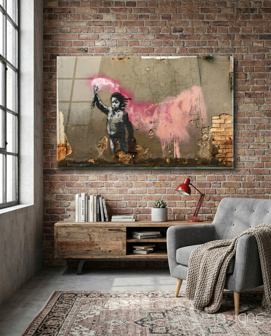Glass art print hung on brick wall above wooden desk in loft room, showing stenciled child figure with pink powder explosion.