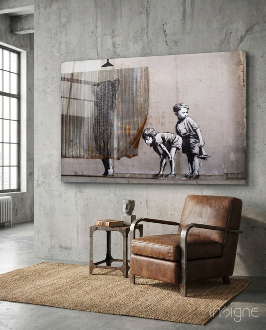 Glass art panel depicting two children watching woman pull back curtain, displayed above leather chair in concrete room.