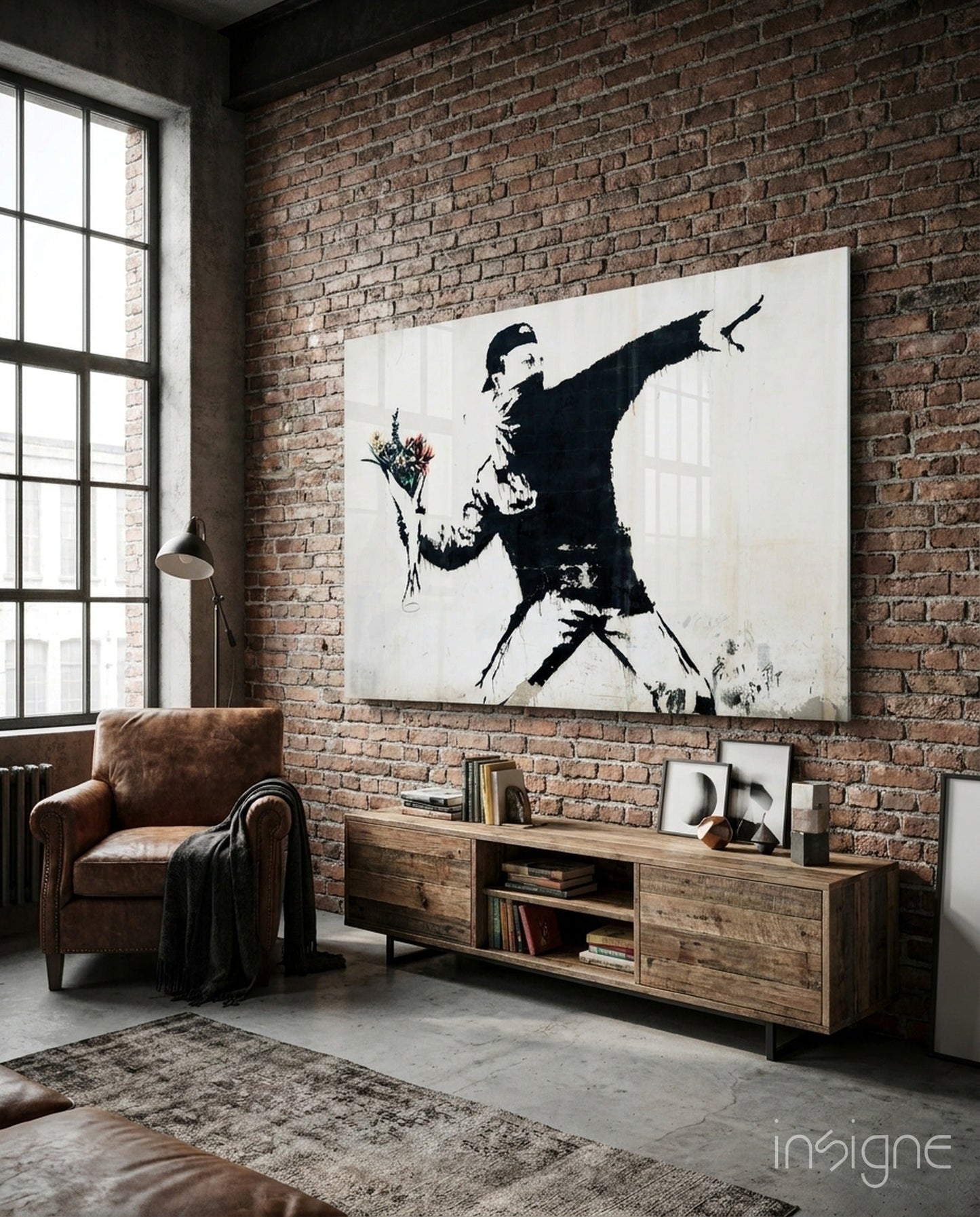 Banksy-style stenciled glass art hanging on exposed brick wall above wooden media console in industrial loft setting.
