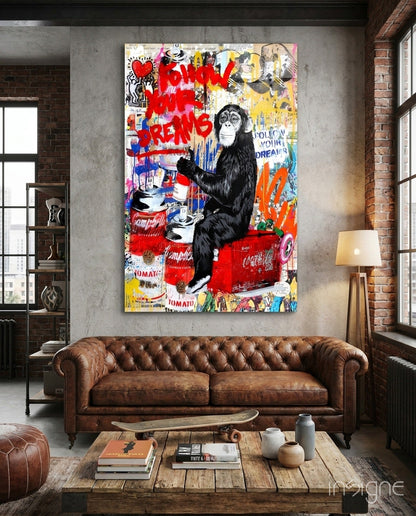 Monkey Advice glass art displayed above a brown leather Chesterfield sofa in an industrial loft space, featuring a black chimpanzee with red spray paint text and Campbell's soup cans.