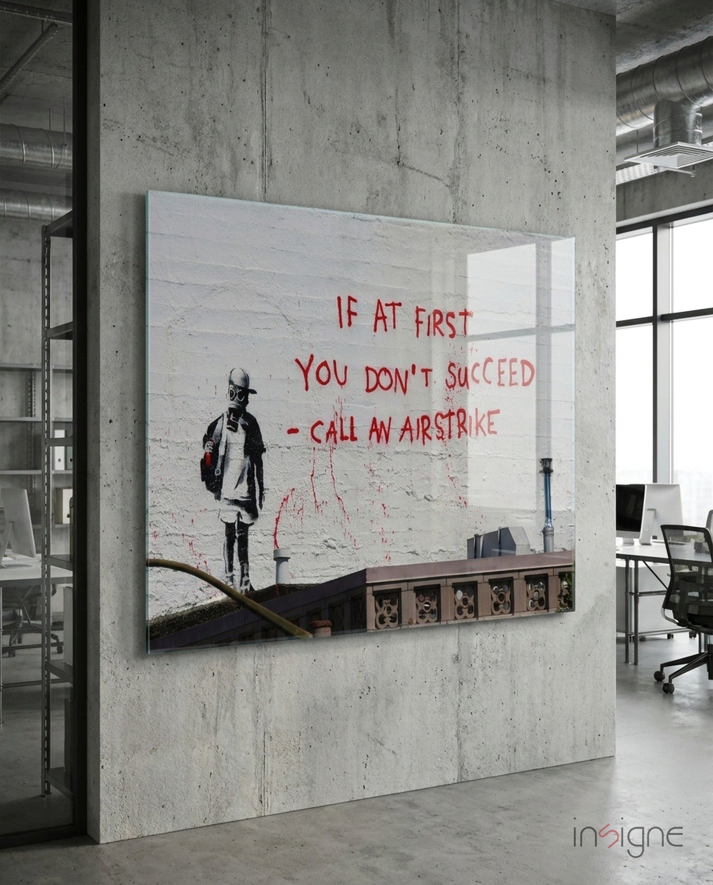 Glass art panel mounted on concrete wall in modern office, featuring stenciled child figure and red text reading "If at first you don't succeed - call an airstrike.