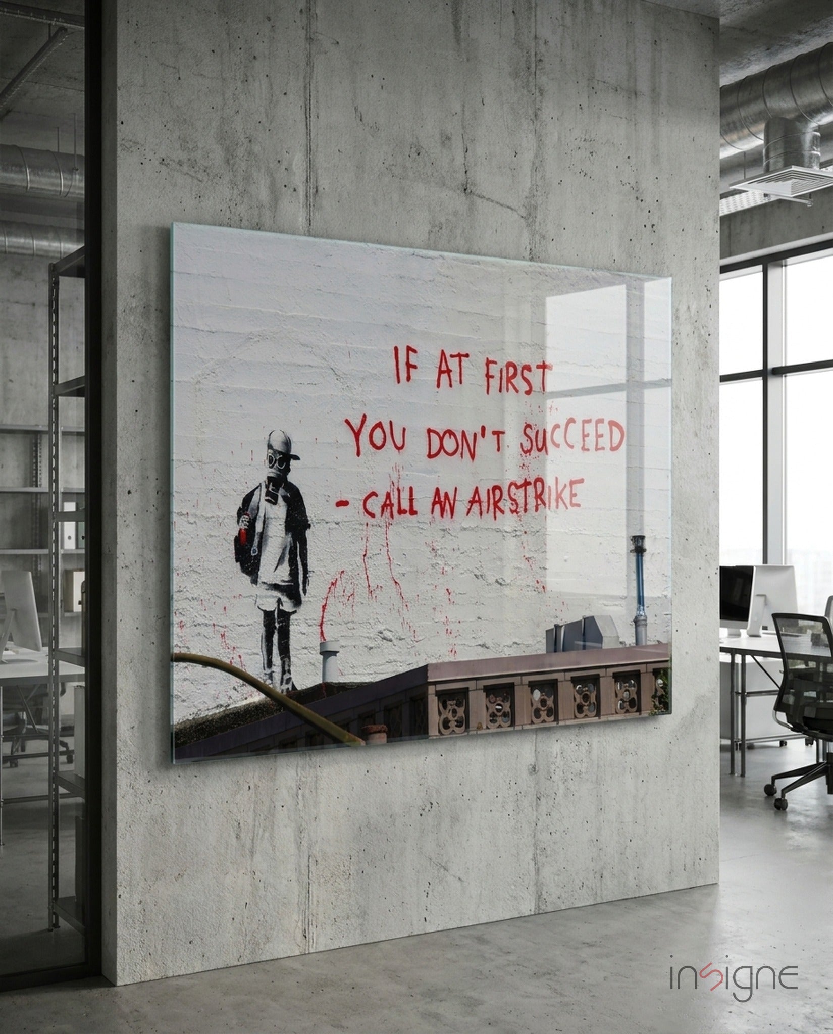 Glass art panel mounted on concrete wall in modern office, featuring stenciled child figure and red text reading "If at first you don't succeed - call an airstrike.