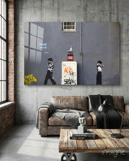 Street art style glass panel featuring silhouetted figures and "FREE DOLLAR" text displayed above brown leather sofa in industrial loft interior.