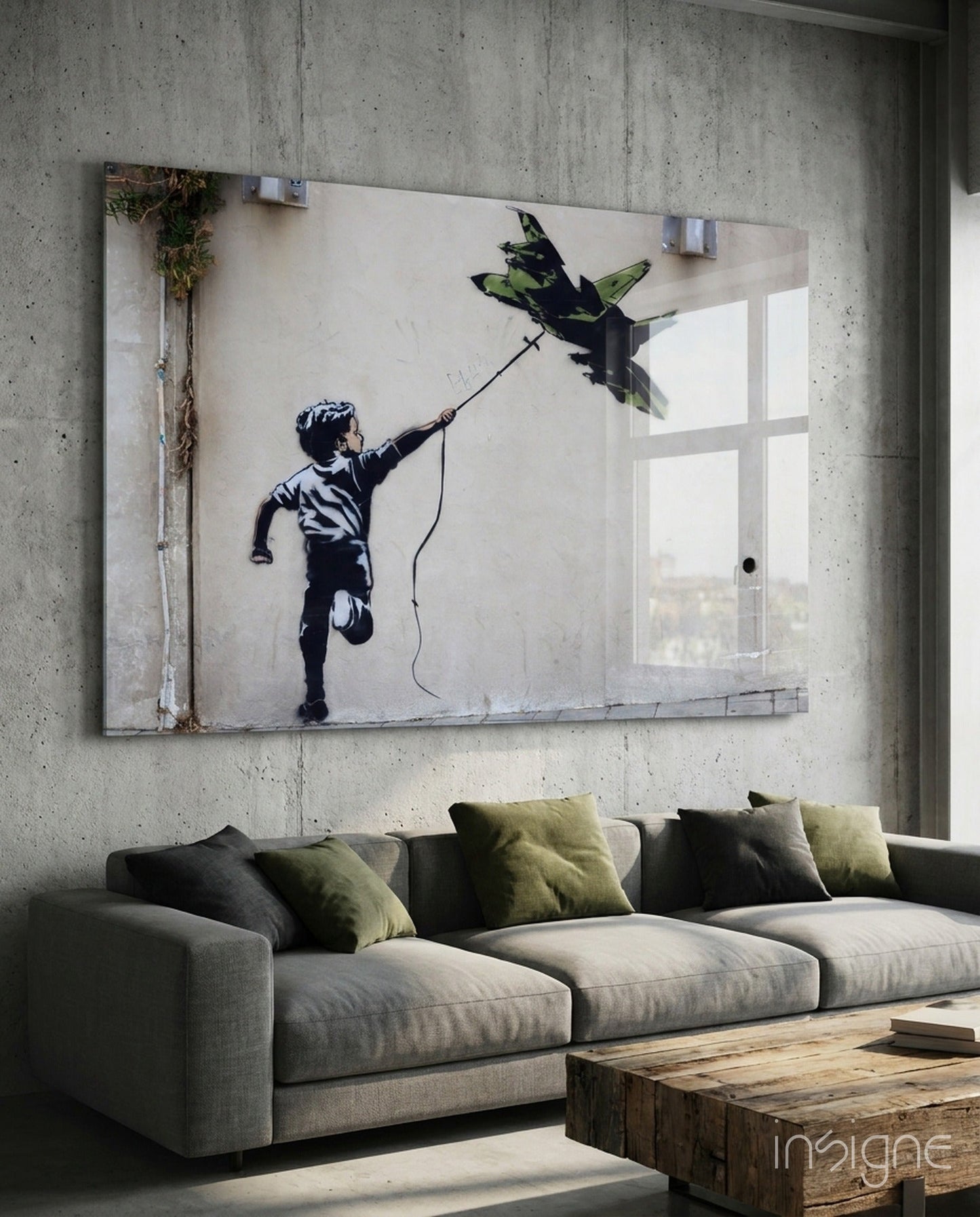 Large glass art panel mounted above gray sofa depicting stenciled silhouette of child flying fighter jet kite.
