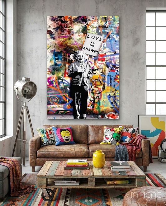 Colorful pop art glass canvas featuring Einstein with "Love is the Answer" banner displayed above brown leather sofa in modern living room.